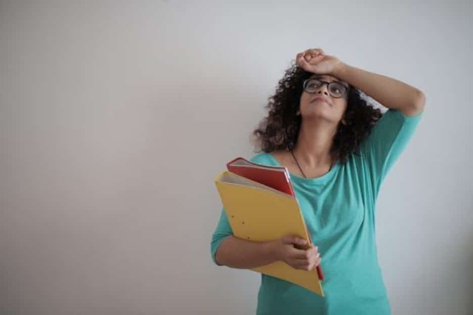 A stressed woman holding red and yellow binders against a white background.